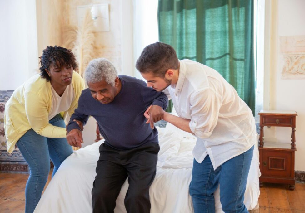 Two caregivers helping elderly man stand